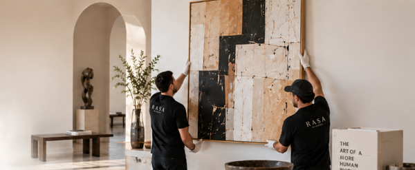 Installers hanging a large abstract painting in a sunlit hallway